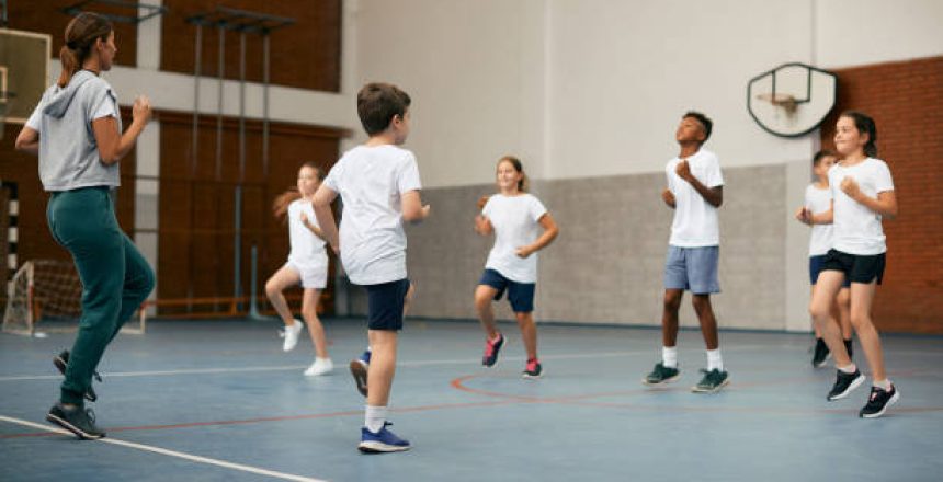 Group of elementary students having PE class with their sports teacher at school gym.